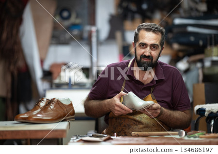 Skilled shoemaker craftsman handcrafting leather shoe in a busy workshop studio 134686197