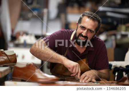 Skilled cobbler crafts leather shoes in a busy workshop, showcasing artisanal leatherwork and craftsmanship. 134686205
