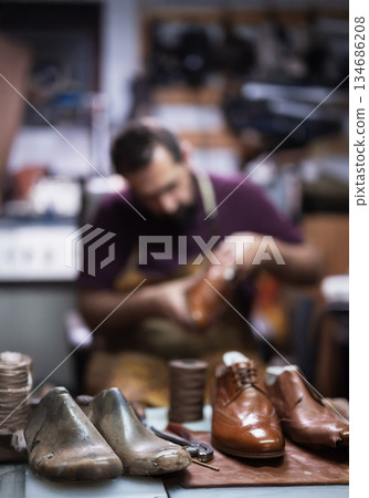 Cobbler at work in a leather shoe workshop shaping brown and metallic shoes with tools 134686208