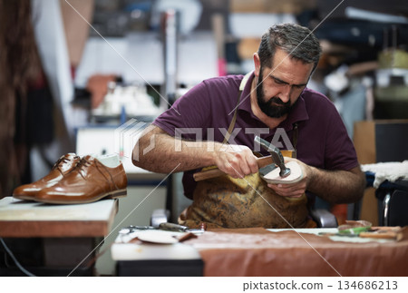 Skilled craftsman shaping a leather shoe in a busy workshop, focused on handcrafting and detail 134686213
