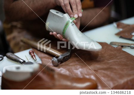 Cobbler measures a prosthetic shoe with a tape measure in a leather workshop Cobbler measures a prosthetic shoe with a tape measure in a leather workshop 134686218