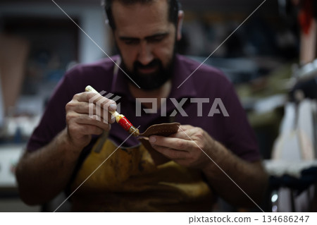 Artisan chocolatier at work, carefully applying glaze to a chocolate piece with a fine brush in a busy workshop 134686247