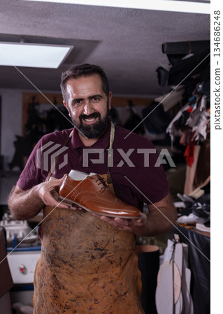 Craftsman shoemaker in his workshop proudly displays a handmade polished brown leather dress shoe 134686248