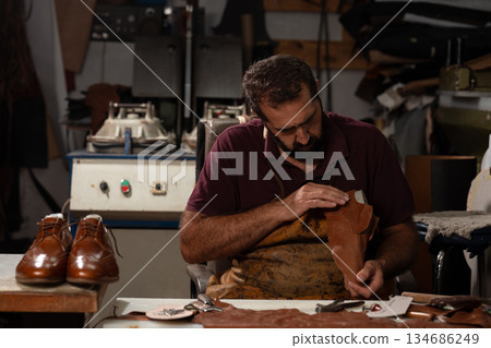 Shoemaker crafts leather shoes in a busy workshop with tools and leather pieces 134686249