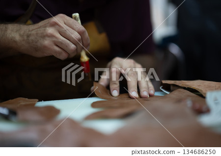 Leather craft in progress: close-up of hands shaping leather pieces with a tool 134686250