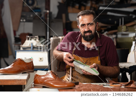 Cobbler at work in a leather workshop, crafting and measuring high-quality shoes 134686262