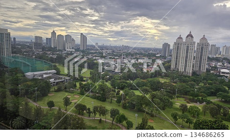 A glowing golf course with sand bunkers and floodlights stretches beneath ornate towers and a vivid sunset, blending sport, architecture, and nature in a dramatic dusk cityscape in Jakarta 134686265