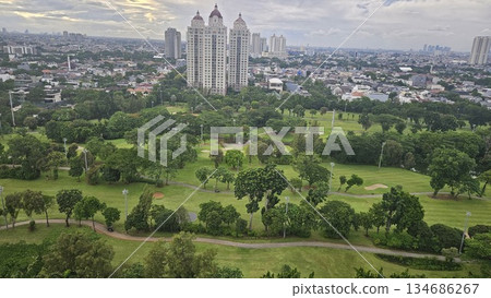 A glowing golf course with sand bunkers and floodlights stretches beneath ornate towers and a vivid sunset, blending sport, architecture, and nature in a dramatic dusk cityscape in Jakarta 134686267