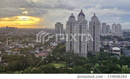 A glowing golf course with sand bunkers and floodlights stretches beneath ornate towers and a vivid sunset, blending sport, architecture, and nature in a dramatic dusk cityscape in Jakarta A glowing golf course with sand bunkers and floodlights stretches beneath ornate towers and a vivid sunset, blending sport, architecture, and nature in a dramatic dusk cityscape in Jakarta 134686269