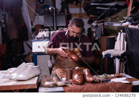 Shoemaker at work crafting leather shoes in a busy workshop with tools and scraps today 134686270