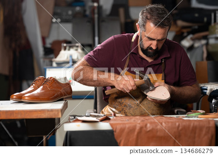 Cobbler at work repairing a leather shoe in a busy workshop Cobbler at work repairing a leather shoe in a busy workshop 134686279
