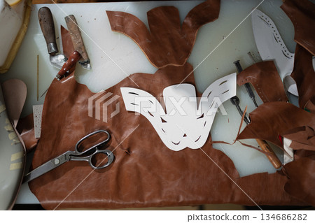 Leather crafting studio with mask templates, tools, and brown leather on a worktable Leather crafting studio with mask templates, tools, and brown leather on a worktable 134686282