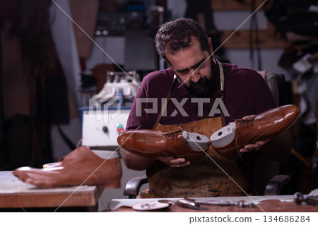 Cobbler at work shaping brown leather shoes in a busy workshop studio Cobbler at work shaping brown leather shoes in a busy workshop studio 134686284
