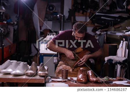 Cobbler at work in a leather workshop crafting a shoe by hand with tools nearby 134686287