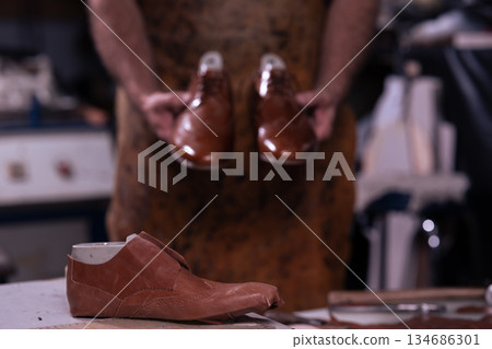 Cobbler holds polished brown leather shoes in a workshop before final fitting 134686301
