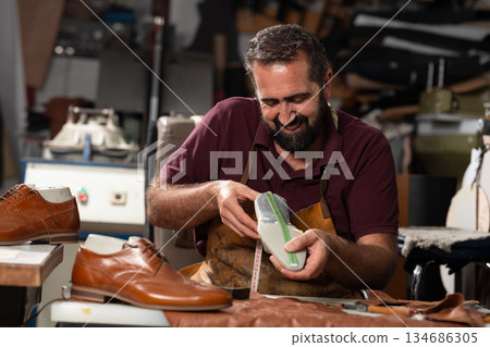 Master craftsman at work polishing and measuring a leather shoe in a busy workshop today Master craftsman at work polishing and measuring a leather shoe in a busy workshop today 134686305