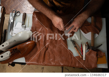 Skilled craftsman sewing leather with tools on a worktable, shoemaking in progress in a workshop studio 134686317