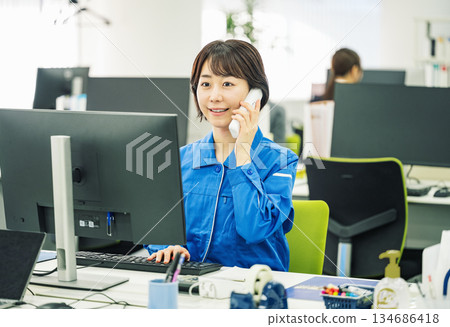 一位身穿工作服的年輕女子正在辦公室接電話。 134686418