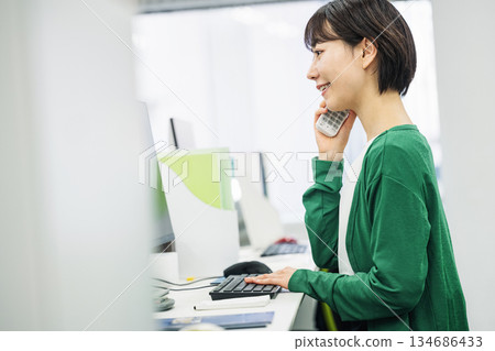 Young woman answering the phone in the office 134686433