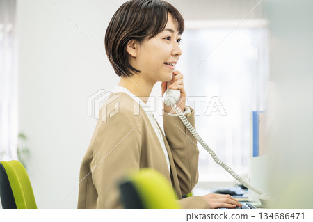 Young woman answering the phone in the office 134686471