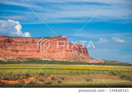 Red Rock Mesa Bluff Rising Above Green Field and Blue Sky 134686581