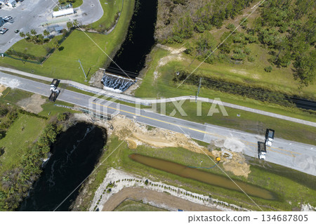 Road construction. Trucks blocking car access at destroyed bridge after hurricane flooding water washed away asphalt in Florida. Safety equipment at roadwork site Road construction. Trucks blocking car access at destroyed bridge after hurricane flooding water washed away asphalt in Florida. Safety equipment at roadwork site 134687805