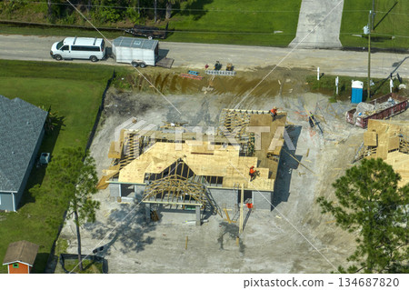 Professional builders working on roof construction of unfinished suburban home with wooden frame structure in Florida rural area. Concept of housing development in America 134687820