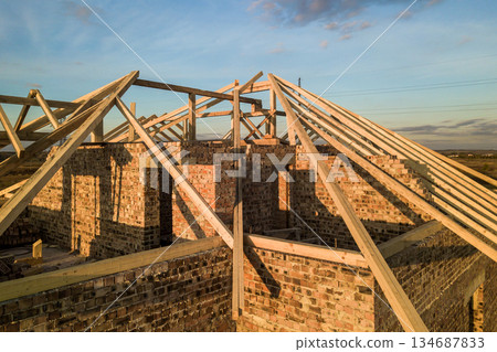 Private residential house with wooden roof frame structure under construction. Unfinished brick building under development. 134687833