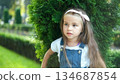Portrait of pretty child girl standing outdoors in green summer park. 134687854