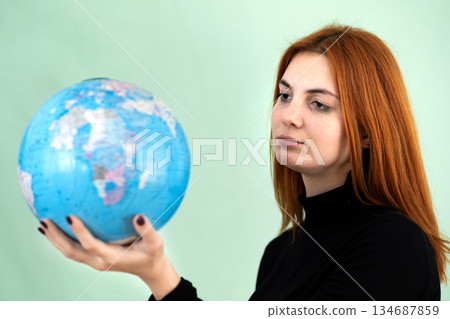 Portrait of a sad worried young woman holding geographic globe of the world in her hands. Travel destination and planet protection concept. Portrait of a sad worried young woman holding geographic globe of the world in her hands. Travel destination and planet protection concept. 134687859