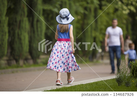 Little child girl in summer dress and a hat walking alone in green park. Little child girl in summer dress and a hat walking alone in green park. 134687926