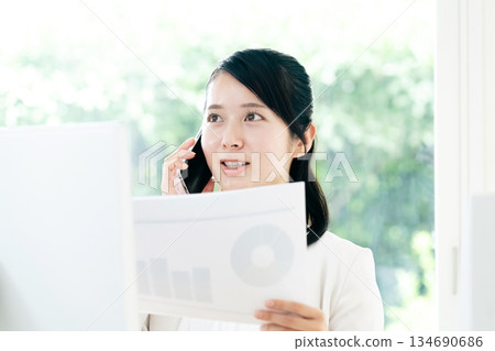 A young woman making a phone call while looking at documents A young woman making a phone call while looking at documents 134690686