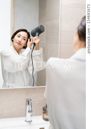 一位女士正在用吹風機吹乾頭髮。美麗的畫面 134691673