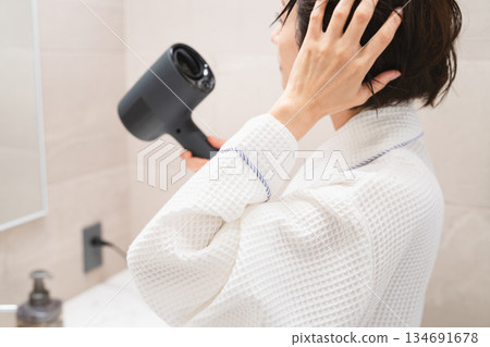 一位女士正在用吹風機吹乾頭髮。美麗的畫面 134691678