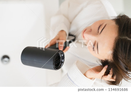 一位女士正在用吹風機吹乾頭髮。美麗的畫面 一位女士正在用吹風機吹乾頭髮。美麗的畫面 134691686