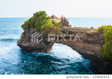 Batu Bolong Temple iconic Hindu shrine on rocky arch along Bali coast attracts travelers with ocean waves, sacred Balinese architecture, Batu Bolong dramatic cliffs, spiritual atmosphere in daylight 134692814