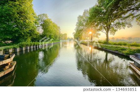 Enjoy a serene morning by the river, surrounded by sunlight and lush trees in nature Enjoy a serene morning by the river, surrounded by sunlight and lush trees in nature 134693851