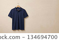 A polo shirt hanging on a wooden hanger against a soft beige textured wall 134694700