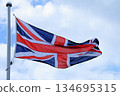The British Union Jack flag flutters powerfully in the wind under a blue sky 134695315