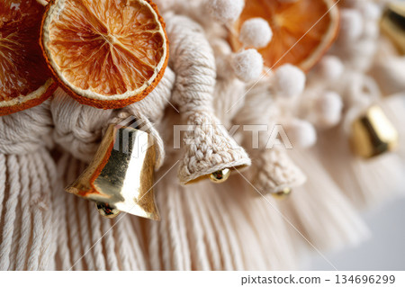 Boho christmas wreath with macrame detail features dried orange slice gold bell and soft pom pom for festive home decor in cozy natural style 134696299