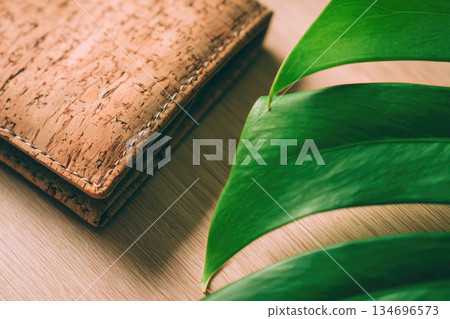 Cork wallet with leather accent displays unique texture on wooden surface beside green leaf creating natural and eco friendly vibe 134696573