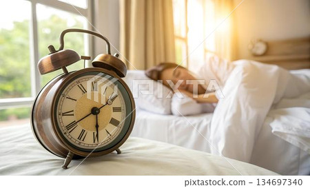 A vintage alarm clock sits beside a person 134697340