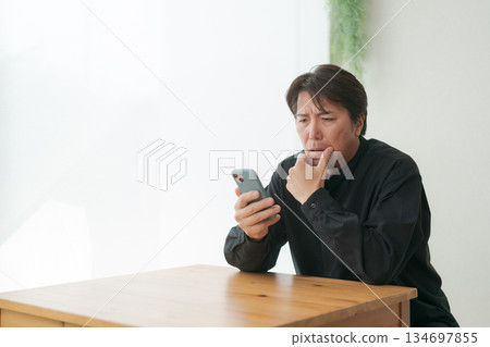 一位中年男子看著他的智慧型手機,感到沮喪。 一位中年男子看著他的智慧型手機,感到沮喪。 134697855