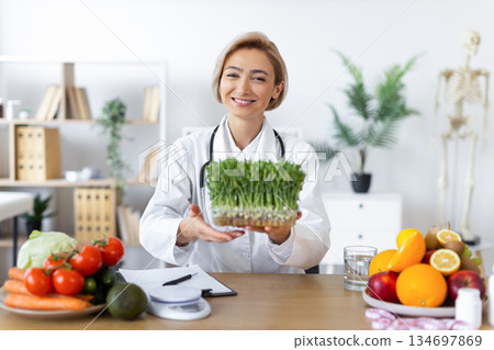 A smiling nutritionist holds a tray of microgreens, surrounded by fresh fruits and vegetables, promoting healthy eating habits. 134697869