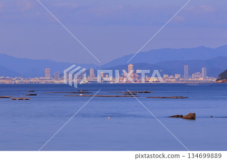黃昏時分的廣島市,從牡蠣養殖筏後方清晰可見。 黃昏時分的廣島市,從牡蠣養殖筏後方清晰可見。 134699889