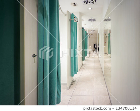Modern retail changing room hallway featuring teal privacy curtains, a reflective mirrored wall, and ceiling ventilation, ready for customer trying clothes 134700114