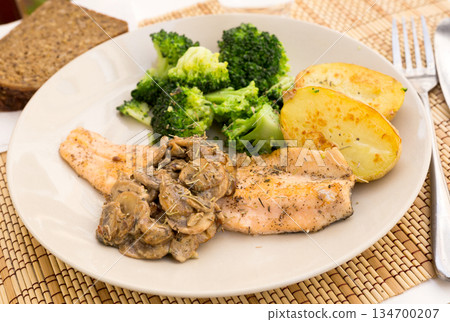fried river trout fillet with a complex side dish of broccoli, baked potatoes and mushroom sauce 134700207