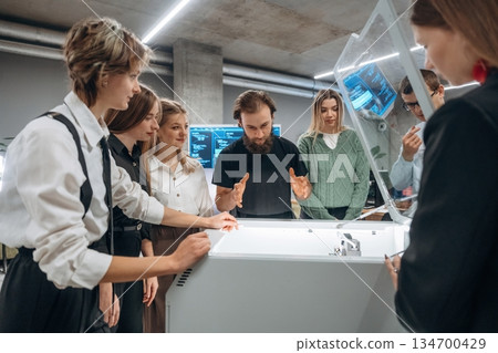 Explaining how the device works. People are in the office by the 3d printer 134700429