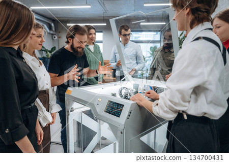 Explaining how the device works. People are in the office by the 3d printer 134700431