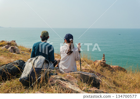 Travel young couple hike mountain, exploring wild nature landscape, enjoying vast ocean view, adventure journey with backpacks, peaceful moment for people overlooking distant horizon Travel young couple hike mountain, exploring wild nature landscape, enjoying vast ocean view, adventure journey with backpacks, peaceful moment for people overlooking distant horizon 134700577